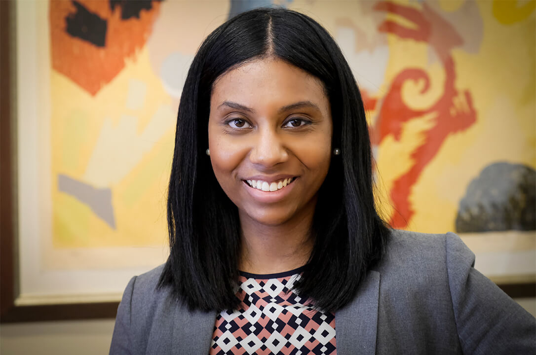 http://Headshot%20of%20Chelsea%20Crawford.%20A%20professional%20headshot%20of%20a%20woman%20with%20straight%20black%20hair,%20wearing%20a%20gray%20blazer%20over%20a%20patterned%20blouse.%20She%20is%20smiling%20and%20looking%20directly%20at%20the%20camera.%20The%20background%20features%20an%20abstract%20painting%20with%20warm%20and%20vibrant%20colors.